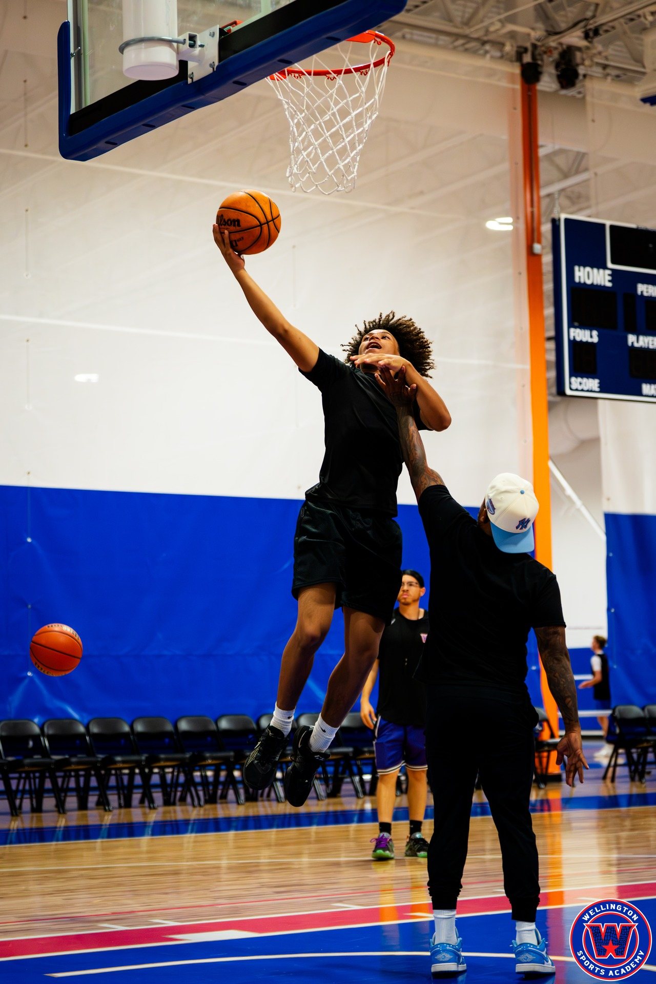 Player leaping for a layup at the basket, coach acting as defender reaching up to contest