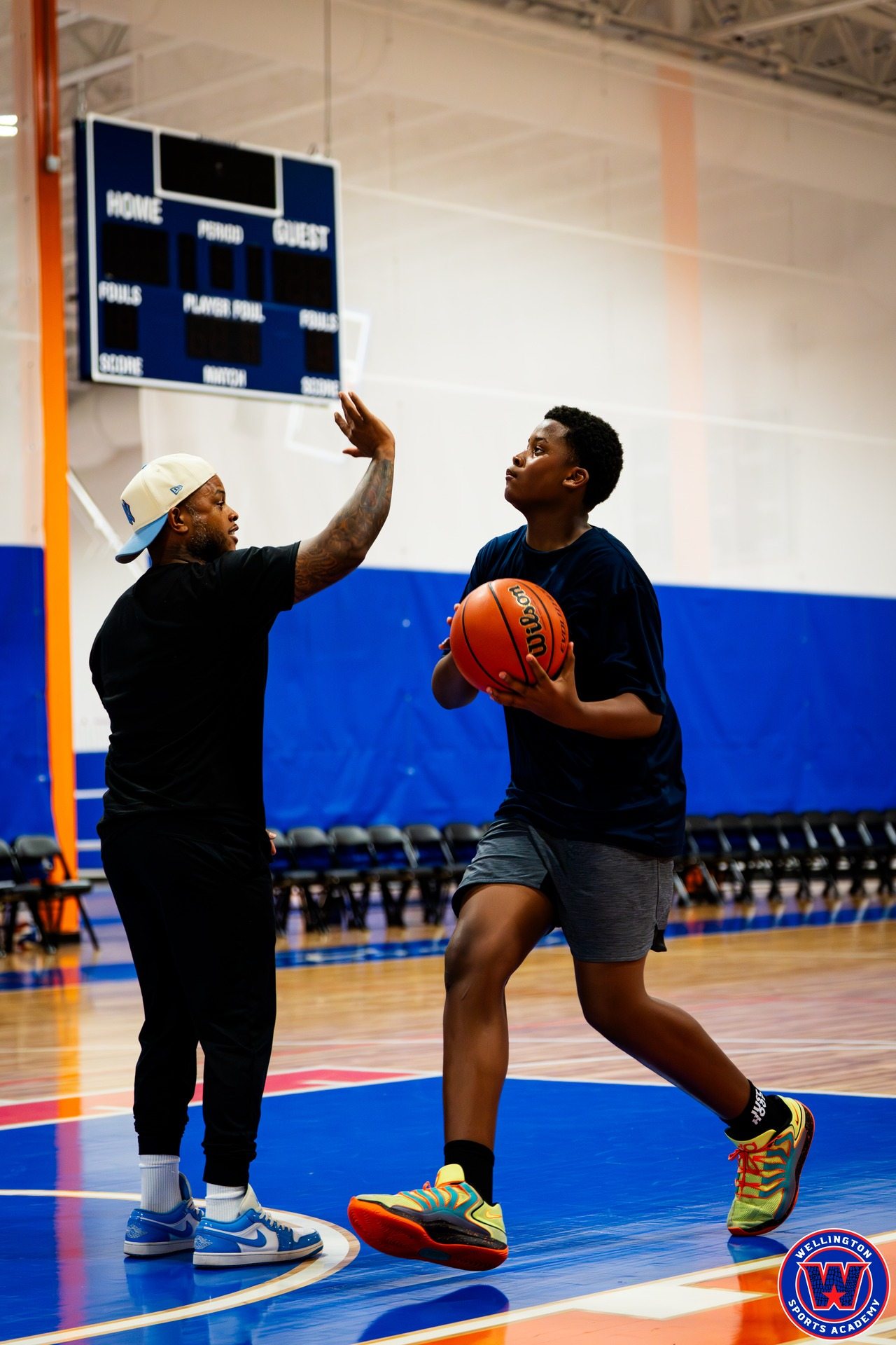 Coach playing active defense with hand up while young player drives with the ball during an offensive drill