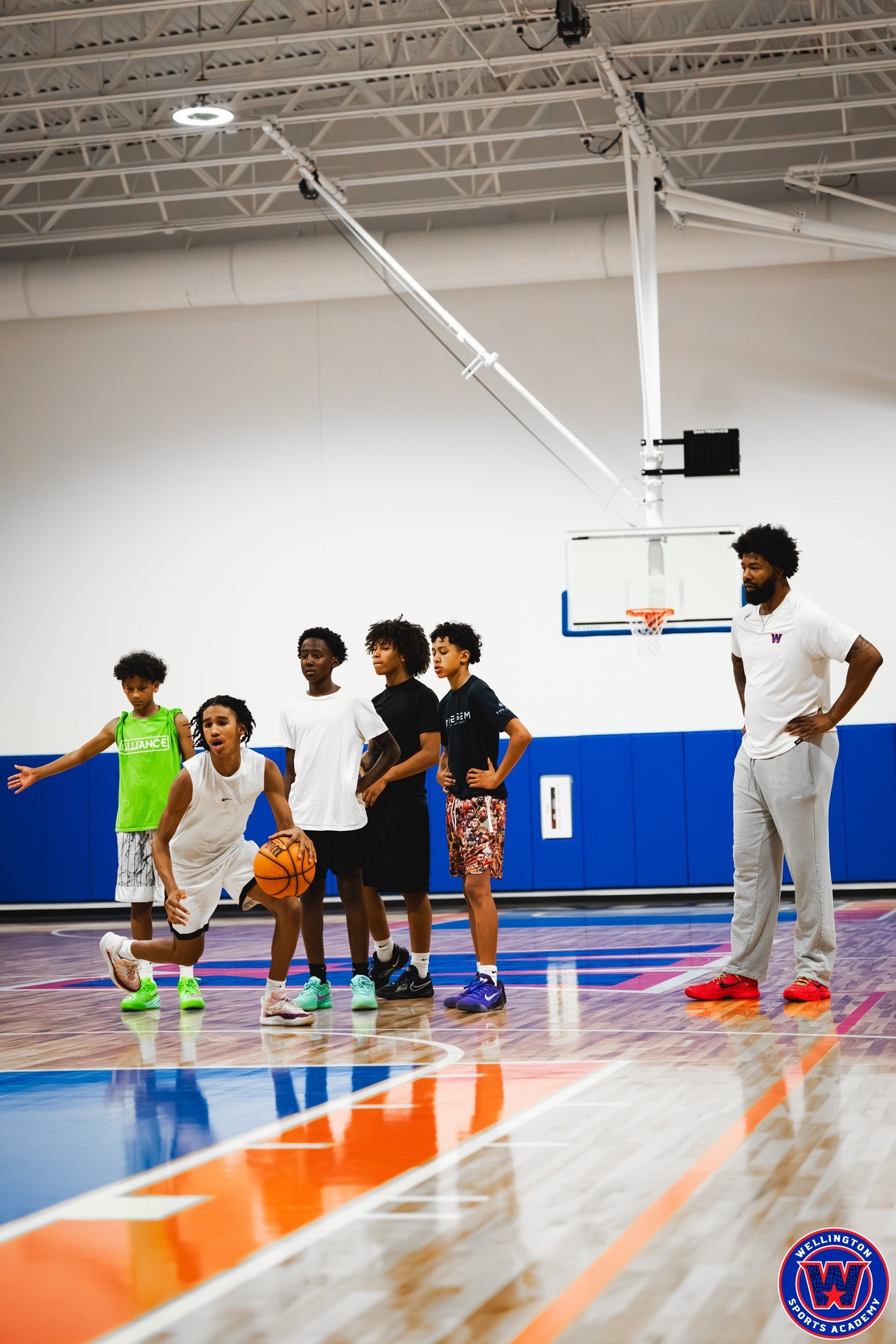 Young player dribbling low near the three-point line while coach and teammates observe