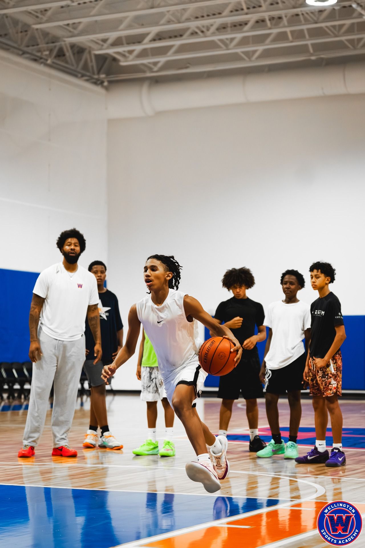 Young player driving forward with the ball during a drill as teammates and coach watch