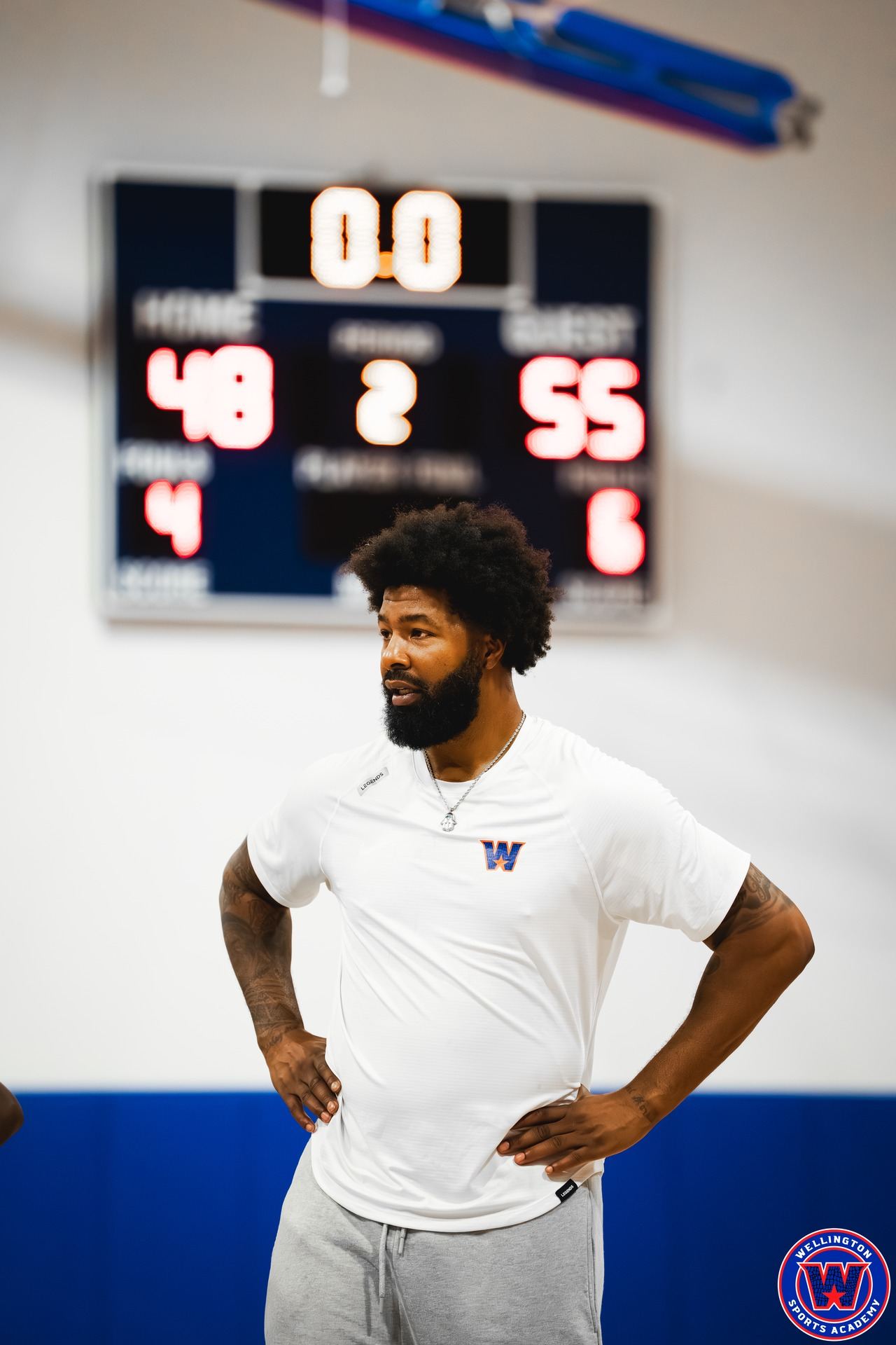 Close portrait of WSA coach in white shirt, scoreboard lit up 48–55 behind him