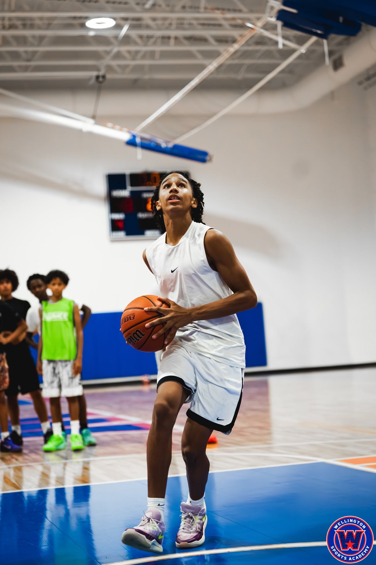 Young player in white Nike kit setting up a shot, eyes on the basket, teammates in background