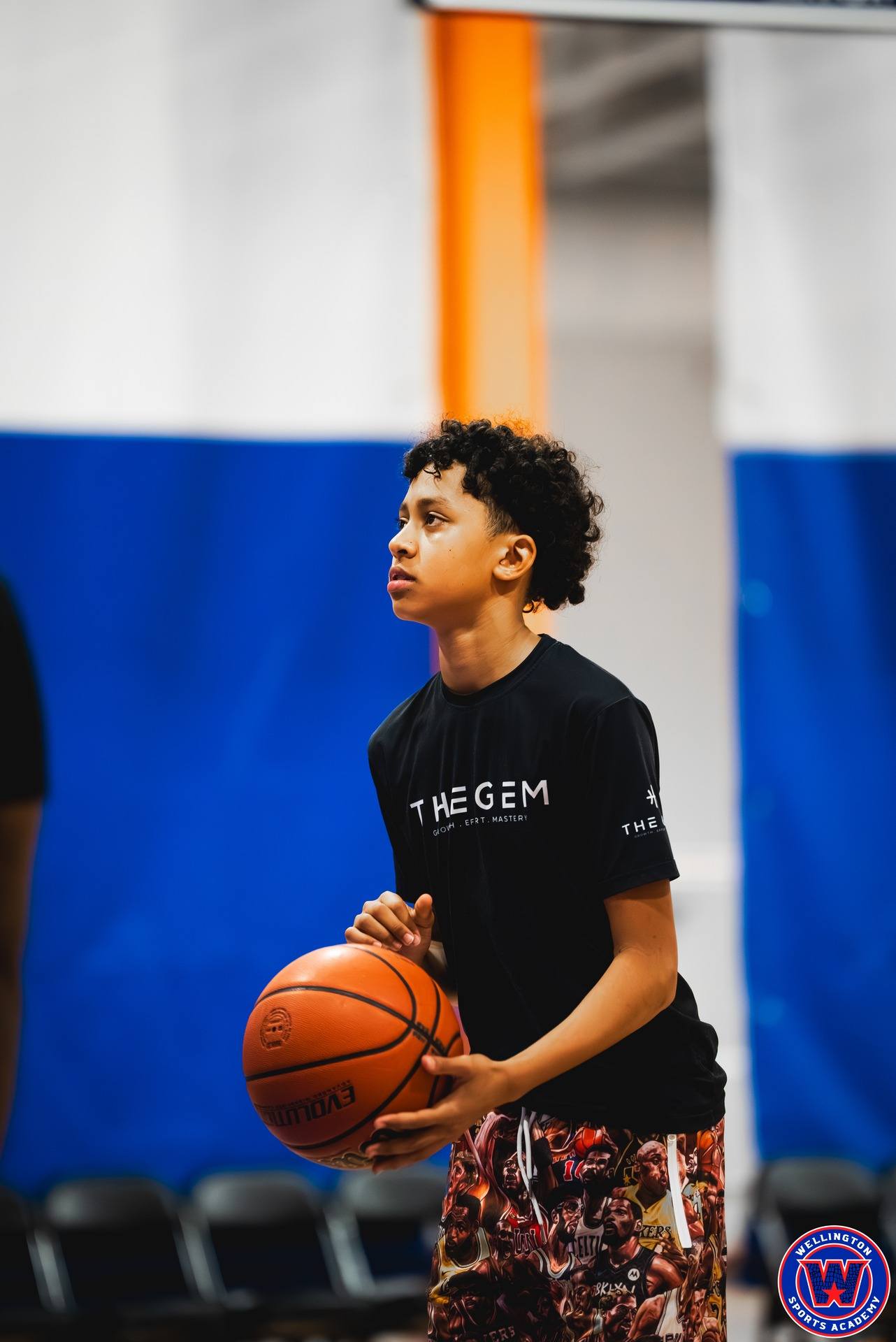 Close-up portrait of young player in black "The Gem" shirt holding a basketball, looking up