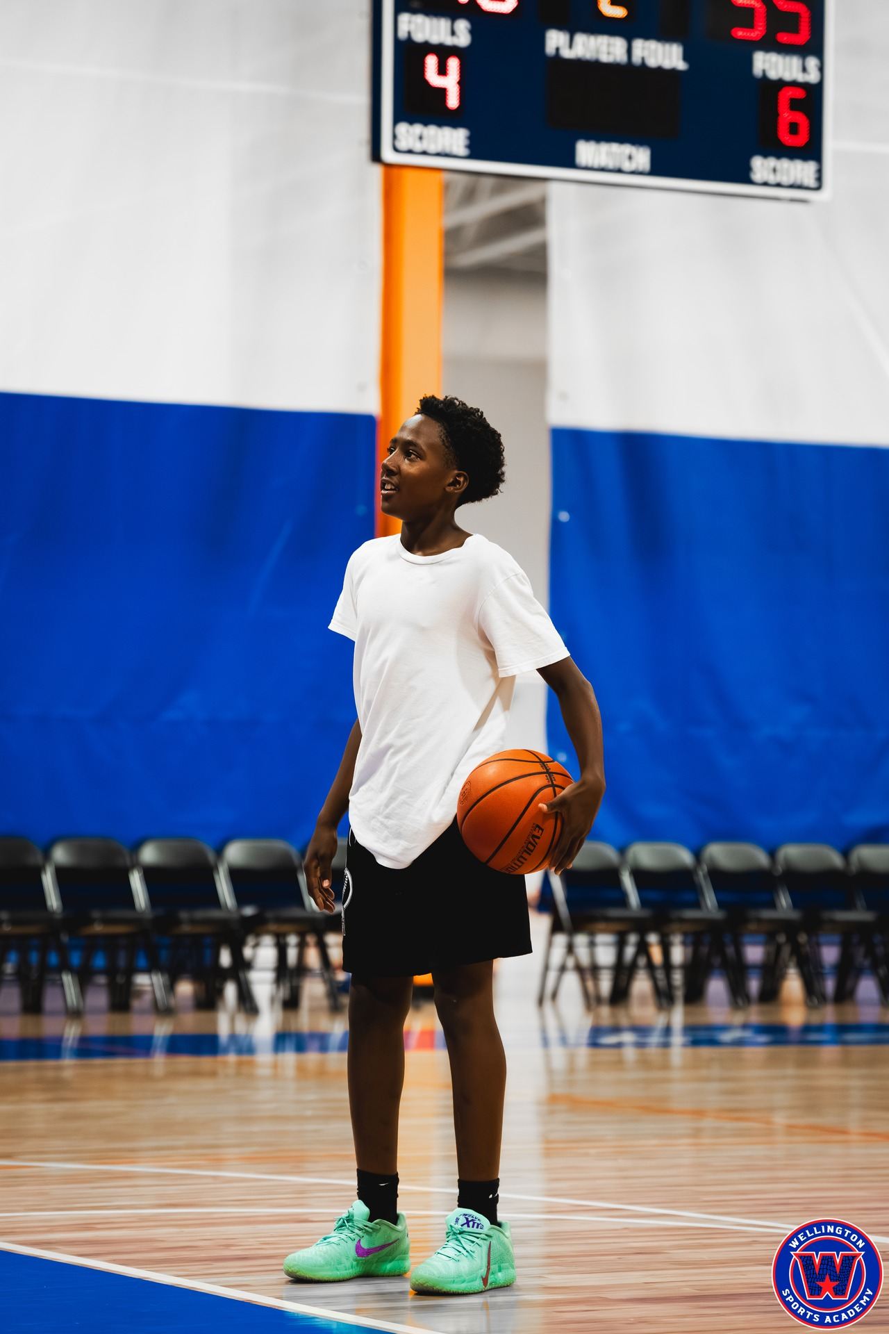 Young player in white standing alone on the court holding a basketball, smiling