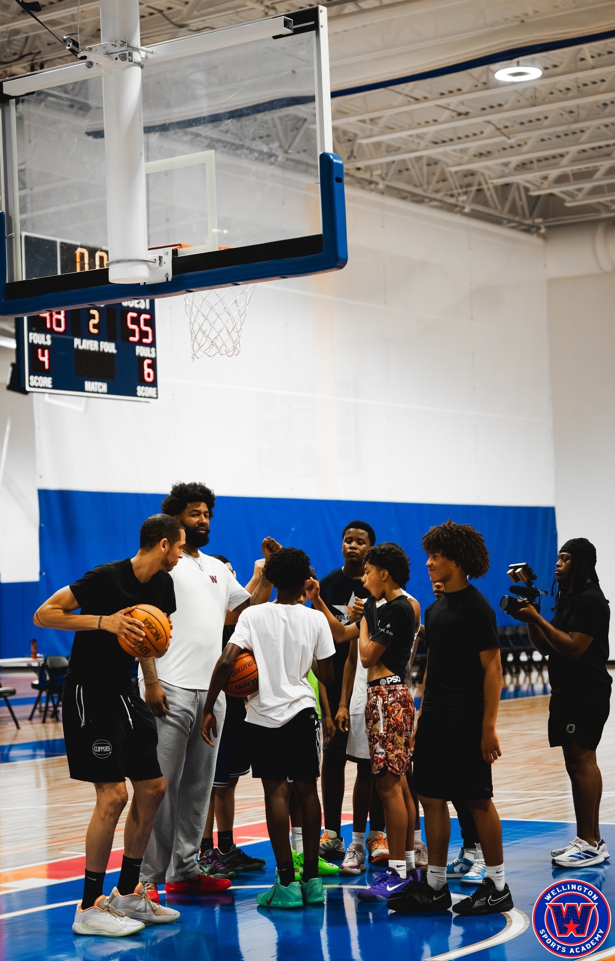 Coaches and players forming a huddle under the basket, camera operator visible at right