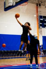 Player leaping for a layup at the basket, coach acting as defender reaching up to contest