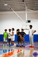WSA coach addressing a group of five young players standing on the court