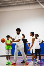 Coach demonstrating a ball-handling move to four attentive young players