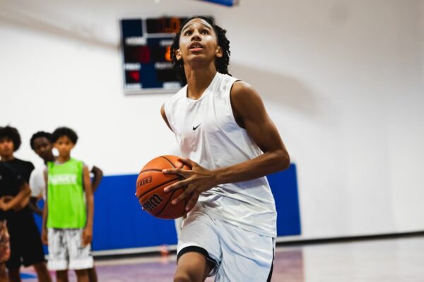 Young player in white Nike kit setting up a shot, eyes on the basket, teammates in background
